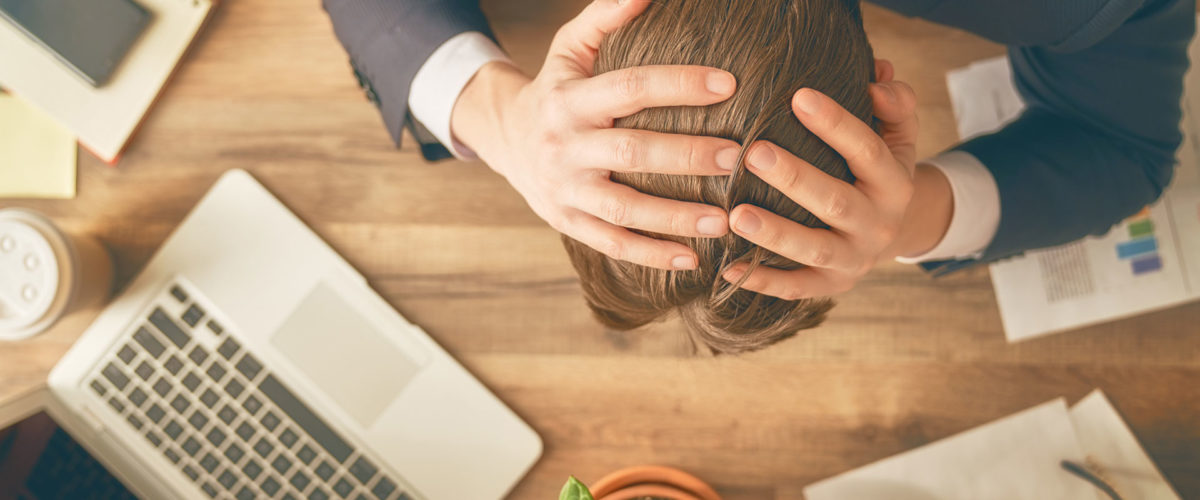 Homme en situation de travail se prenant la tête avec ses mains face à un problème